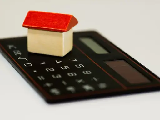 Maisonnette en bois sur calculatrice, symbolisant la régularisation de charges locatives tardives.