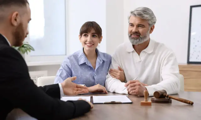 Un couple signe des documents, possiblement un justificatif de propriété, avec un avocat.