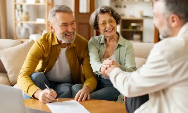 Couple âgé souriant discutant avec un conseiller, signature d'un prêt relais senior.