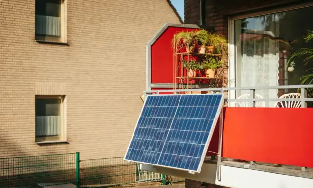 Panneau solaire sur un balcon rouge, peut-être pour contester une augmentation de loyer liée au DPE.