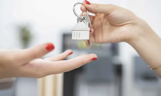 Une main tend des clés avec un pendentif maison. Le locataire reçoit les clés, prêt à emménager et à gérer ses impôts locaux.