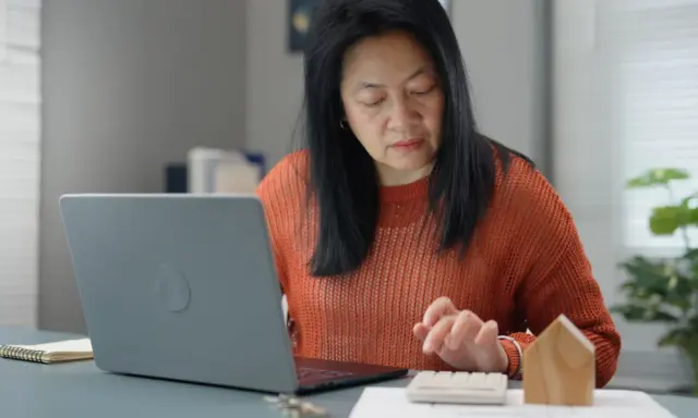 Femme calculant des frais de location avec un ordinateur portable et une calculatrice.