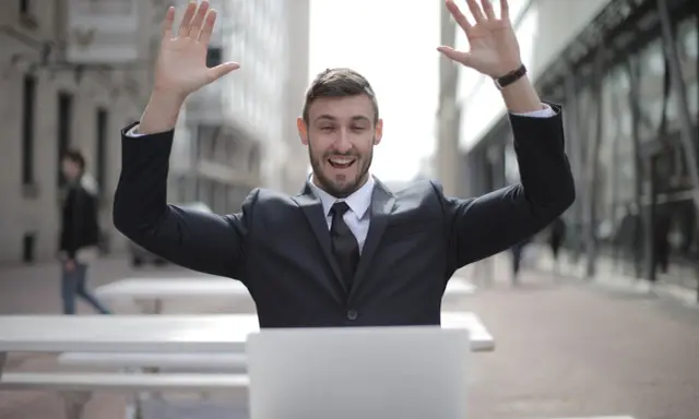 Homme en costume, bras levés, devant un ordinateur. Il semble avoir trouvé quel salaire pour emprunter 400 000 euros.
