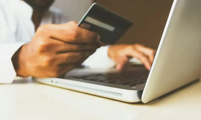 Homme utilisant une carte bancaire sur un ordinateur portable pour configurer un virement automatique de loyer avec son RIB.