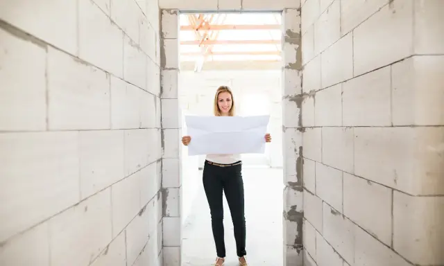 Femme souriante tenant un plan dans un chantier. Un acompte encaissé pour des travaux non réalisés, mais l'espoir est là.