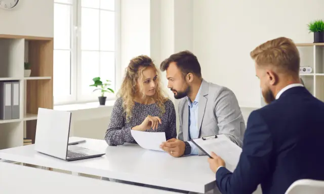 Un couple discute de documents avec un conseiller. Ils cherchent des solutions pour leur reste à vivre, une personne.