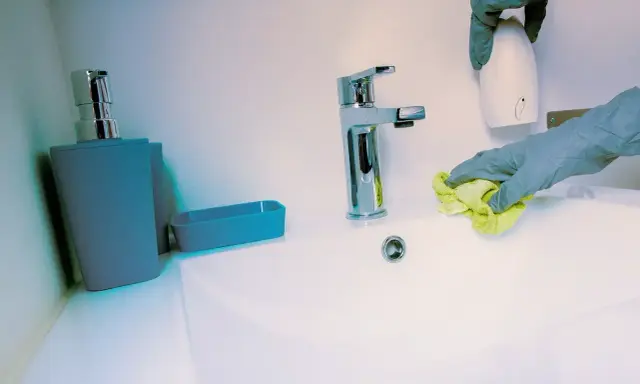Mains de nettoyage avec un chiffon jaune, une retenue sur caution pour nettoyage. Un distributeur de savon et un robinet chromé sont visibles.