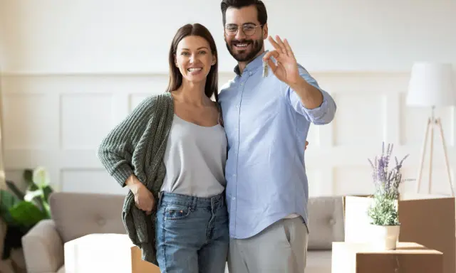 Couple heureux tenant les clés de leur nouvelle maison. L'homme fait le signe OK, symbolisant la réussite de leur projet immobilier, sans annulation offre d'achat par l'acheteur.
