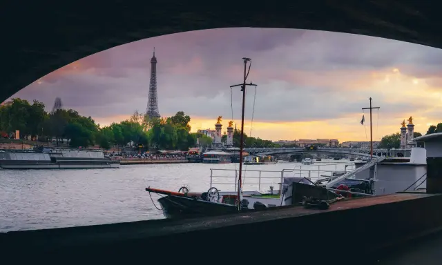 Vue de Paris au coucher du soleil, avec la Tour Eiffel en arrière-plan. Une péniche est amarrée, offrant un aperçu de la vie sur l'eau.