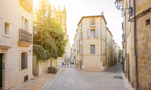 Ruelles pavées et bâtiments ocres, un aperçu des meilleurs quartiers de Montpellier. Des vélos attendent, des passants flânent sous le soleil.