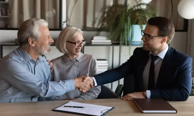 Un couple âgé serre la main d'un homme en costume. Ils sont co-emprunteurs mais pas propriétaires, un accord financier est signé.