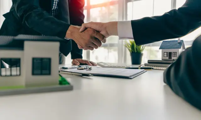Poignée de main entre deux hommes d'affaires, symbolisant la réussite de la vente de son appartement. Maquettes de maisons sur la table.