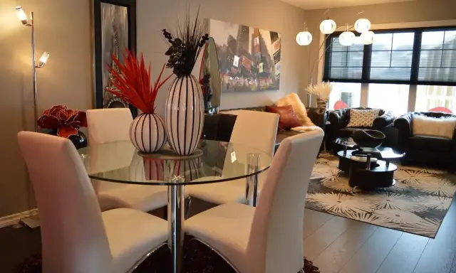 Table à manger moderne avec chaises blanches, parfaite pour une lmnp residence secondaire. Salon cosy avec canapés en cuir et tapis graphique.