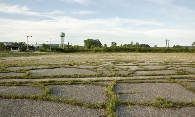 Vaste terrain vague avec des dalles de béton craquelées envahies par l'herbe. Idéal pour réfléchir à ce que peut on faire sur un terrain non constructible.