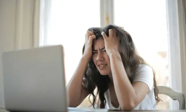 Jeune femme stressée devant son ordinateur, confrontée à la complexité de la réglementation d'une location saisonnière.