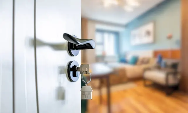 Clé sur la serrure d'une porte ouverte sur un salon. Le locataire peut exercer son droit de préemption si le prix baisse.