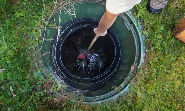 Vidange fosse septique avant le départ du locataire. Un homme utilise un outil pour nettoyer le fond de la fosse.