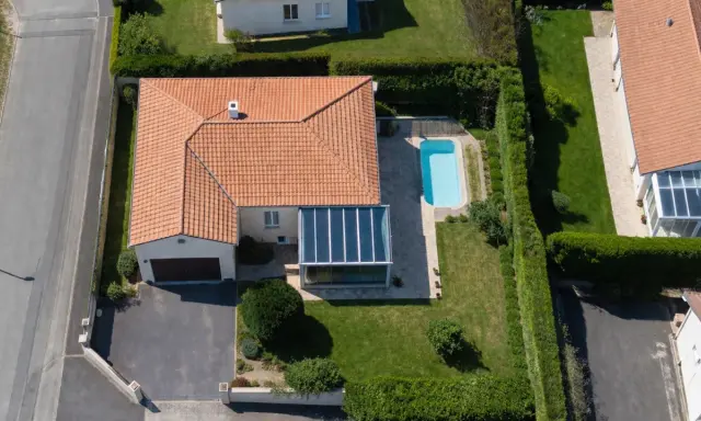 Vue aérienne d'une maison avec piscine et véranda. Une dépendance maison impôts, un garage et une allée complètent le paysage.