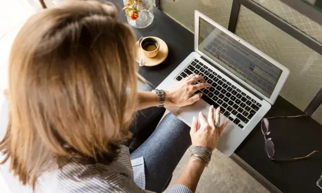 Femme tapant sur un ordinateur portable, une tasse de café à côté. Elle rédige peut-être une lettre recommandation locataire.