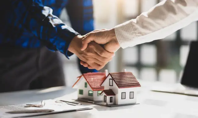 Poignée de main sur des maquettes de maisons, symbolisant un accord. Le compromis de vente délai dépassé par le vendeur est une préoccupation.