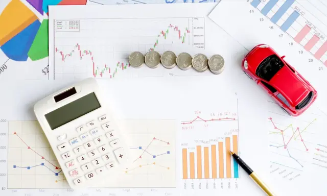 Calculatrice, pièces et voiture rouge sur des graphiques financiers. Idéal pour illustrer les frais de remboursement anticipé prêt immobilier.