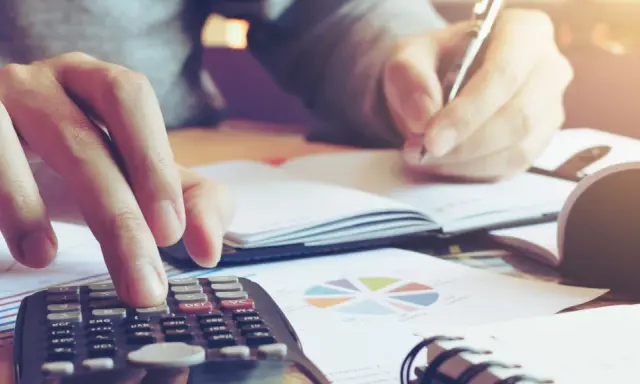 Calculatrice et stylo en main, une personne travaille sur un tableau d'amortissement d'un bien immobilier, entourée de graphiques.