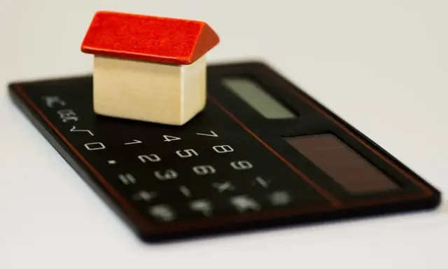 Maisonnette en bois sur calculatrice, symbolisant la régularisation de charges locatives tardives.