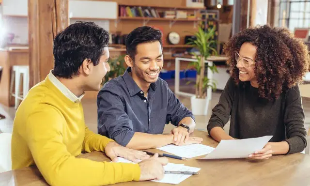 Trois personnes discutent autour d'une table, examinant des documents. Ils semblent planifier leur projet et se demandent combien emprunter avec 2500 euros par mois.