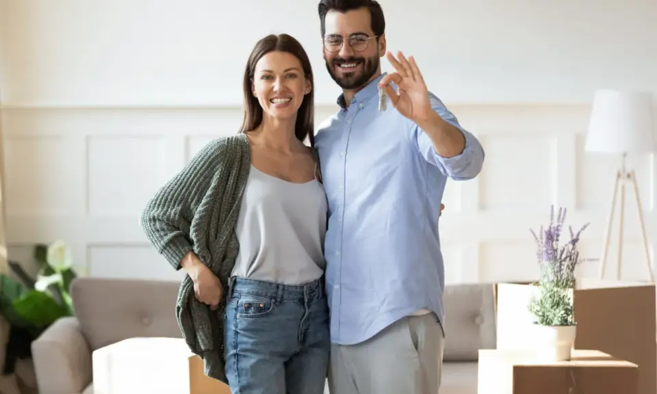 Couple heureux tenant les clés de leur nouvelle maison. L'homme fait le signe OK, symbolisant la réussite de leur projet immobilier, sans annulation offre d'achat par l'acheteur.