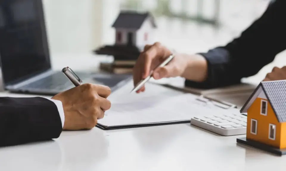 Signature d'un accord pour la résiliation d'un mandat exclusif après 3 mois. Des maisons miniatures et un ordinateur sont visibles.