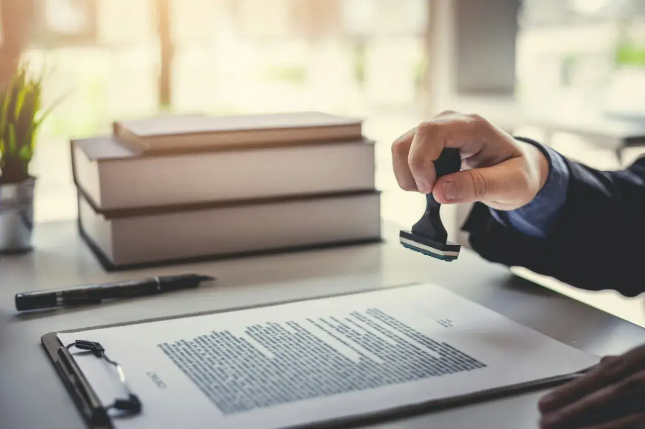 Main d'une personne apposant un tampon sur un document, scellant ainsi un titre de propriété.