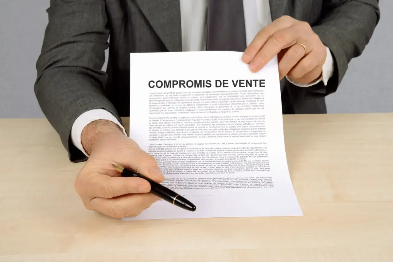 Un homme en costume gris présente un compromis de vente avec un stylo à la main, prêt à signer.