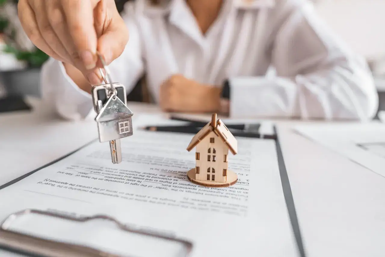 Une main présente une clé avec un pendentif en forme de maison sur un contrat, symbolisant le droit de préemption dans une transaction immobilière.