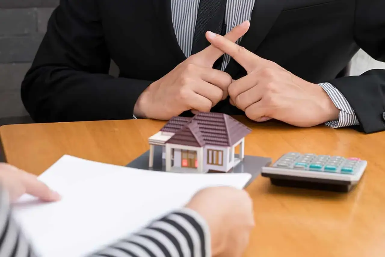 Mains crois&eacute;es, symbole de refus. Le nombre de refus de banque pour annuler un compromis est une pr&eacute;occupation. Une calculatrice et une maquette de maison sont sur la table.