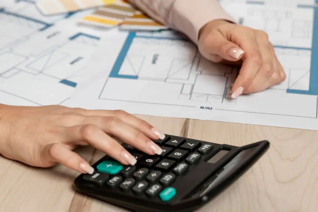 Calculatrice et plans d'architecte. Une main pianote sur la calculatrice, l'autre pointe un d&eacute;tail du plan, peut-&ecirc;tre pour une exon&eacute;ration plus-value indivision.