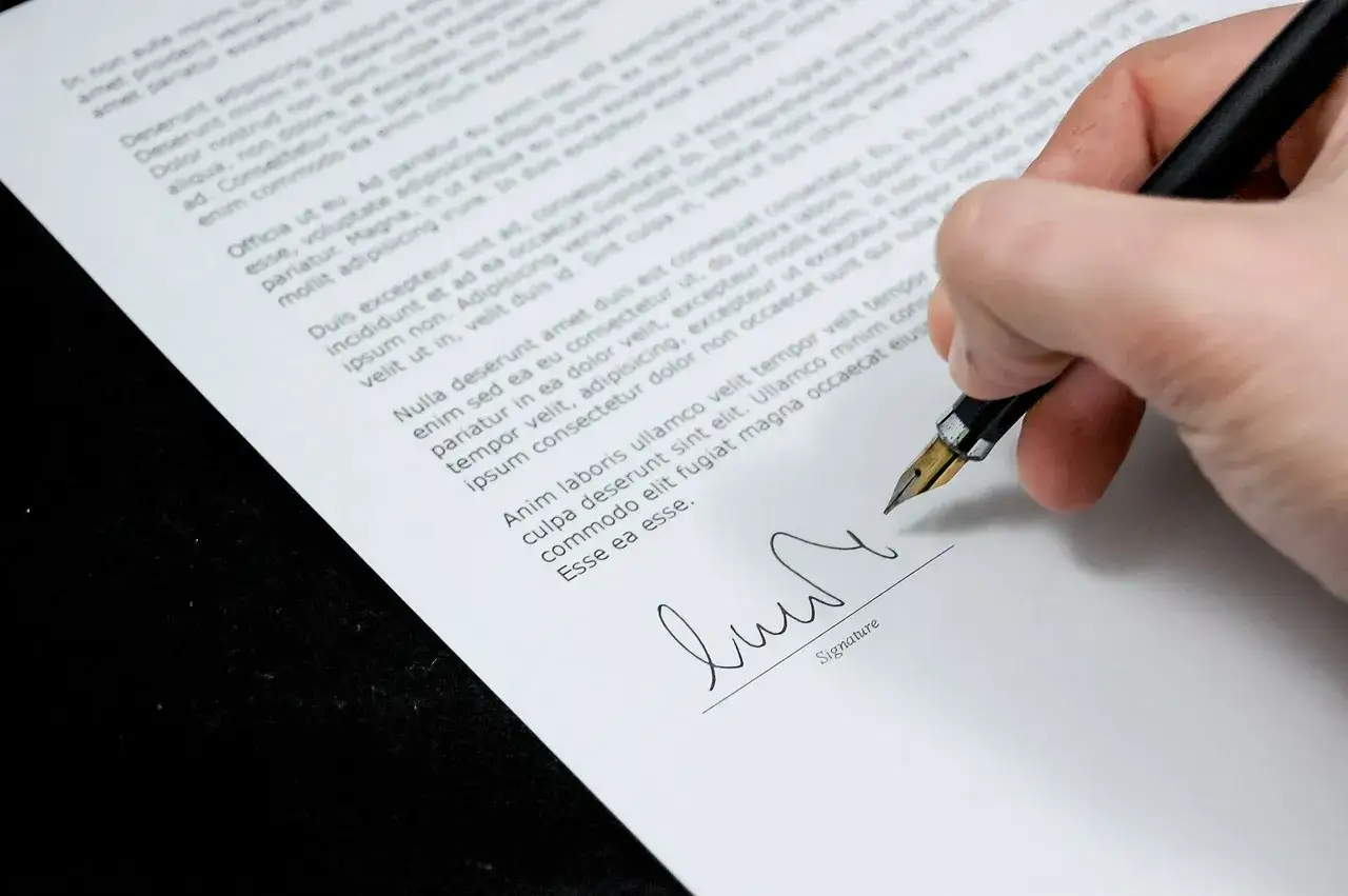 Main d'une personne signant un document, peut-être un titre de propriété, avec un stylo plume.
