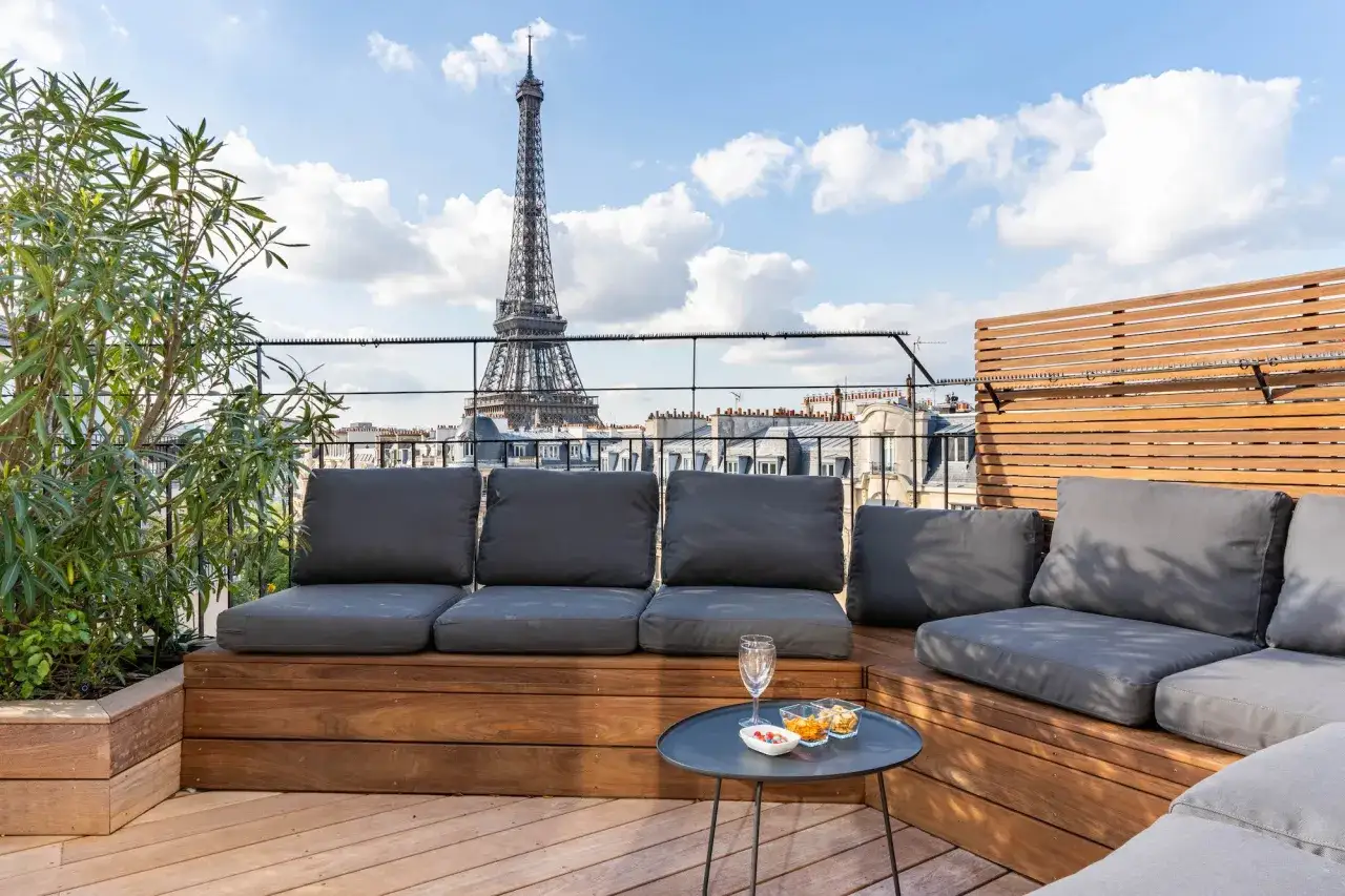 Terrasse parisienne avec vue sur la Tour Eiffel. Canap&eacute;s confortables, table basse avec ap&eacute;ritifs. Un vrai compl&eacute;ment de loyer pour profiter de la vie parisienne.