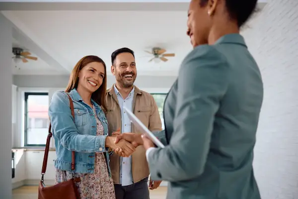 Un couple heureux serre la main d'une agente immobilière. Ils ont trouvé leur nouveau chez-soi, espérant que le loyer ne dépasse pas 3x leur salaire brut.