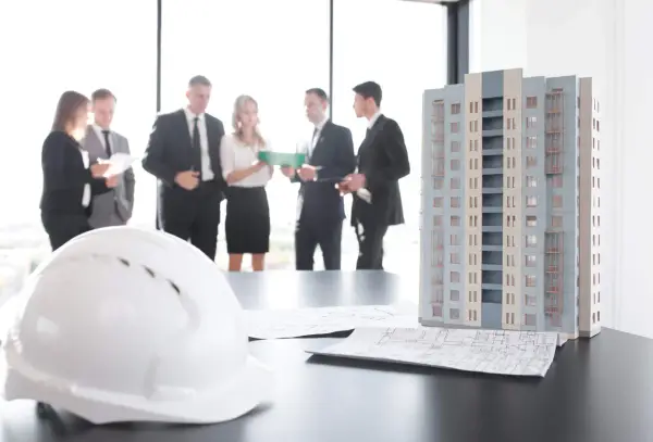 Maquette d'immeuble, plans et casque blanc sur une table. Des professionnels discutent, peut-être des travaux sur parties communes sans autorisation.
