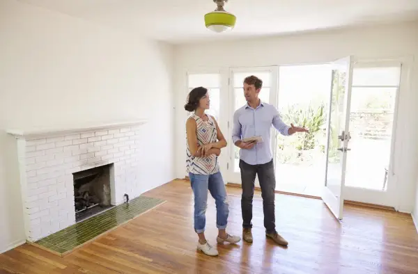 Un agent immobilier présente un appartement ou une maison à une cliente potentielle. La pièce est lumineuse, avec une cheminée en briques blanches et un sol en bois.