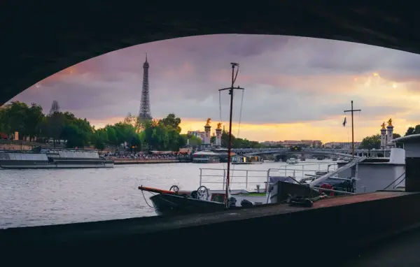 Vue de Paris au coucher du soleil, avec la Tour Eiffel en arrière-plan. Une péniche est amarrée, offrant un aperçu de la vie sur l'eau.