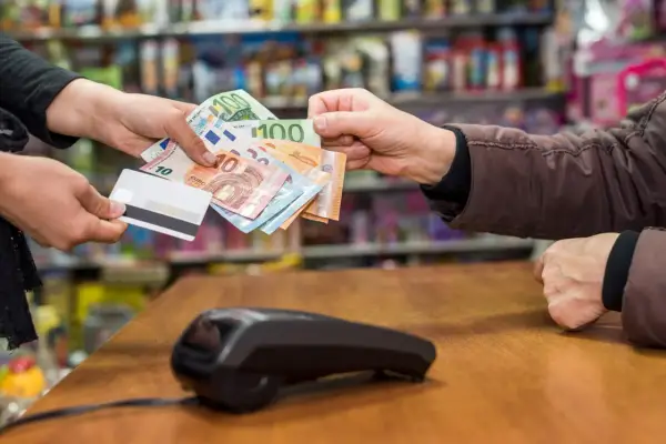 Une main tend des billets en euros et une carte bancaire. La question est : peut-on payer un artisan en liquide ?