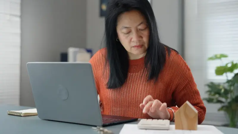 Femme calculant des frais de location avec un ordinateur portable et une calculatrice.